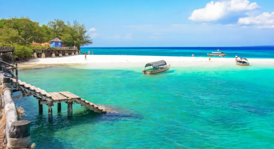 Zanzibar - wczasy opinie: turkusowa woda, biała plaża, drewniany pomost i łodzie. Rajskie widoki idealne na wakacje.