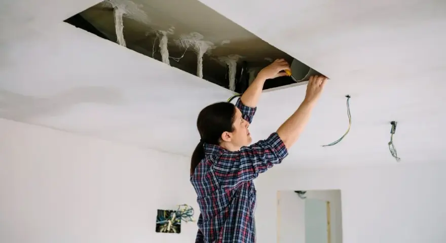 Kobieta pracuje przy suficie podwieszanym, sprawdzając rozstaw profili i instalację elektryczną.
