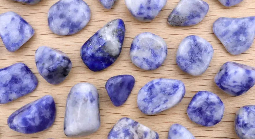 Tumbled sodalite stones, showcasing their deep blue and white patterns. Le pietre di sodalite, con le loro proprietà calmanti, sono disposte su un fondo di legno.