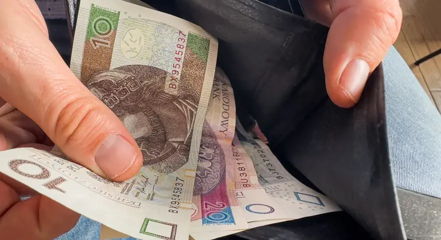 Ręka wyciąga polskie banknoty z portfela. Czy to wyjaśnia, dlaczego w marcu 2026 r. limity dochodowe do dodatku mieszkaniowego wzrosły o 20 proc.?