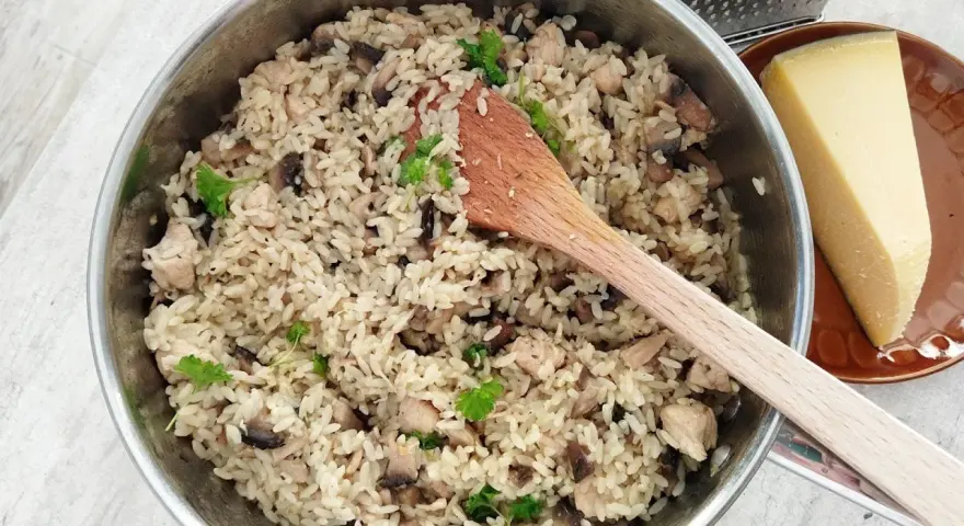 Kremowe risotto z pieczarkami i kurczakiem w garnku, obok kawałek parmezanu i tarka.