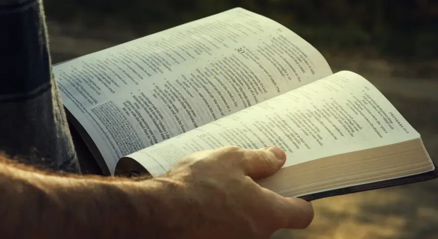 A hand holds open a Bible, revealing the words of Agur in the Bible, Proverbs 31:2.