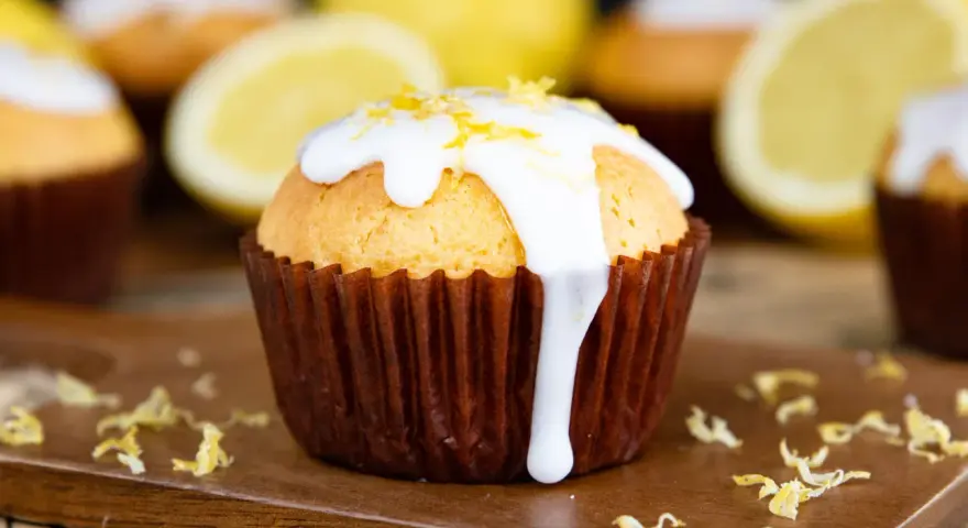 Zitronenmuffins mit weißer Glasur und Zitronenschale, die an eine Backmischung für Zitronenmuffins erinnern.