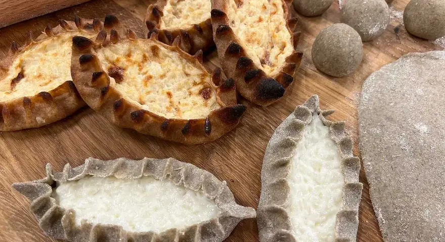 Färdiga piroger och ingredienser för piroger recept. Degbollar, kavlad deg och nybakade piroger med ostfyllning.
