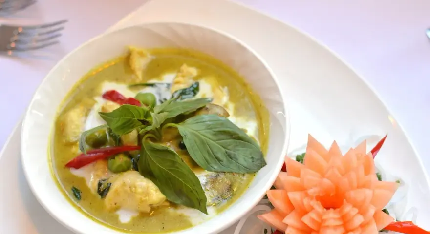 Zielone curry z kurczakiem, ozdobione bazylią i kwiatkiem z marchewki.