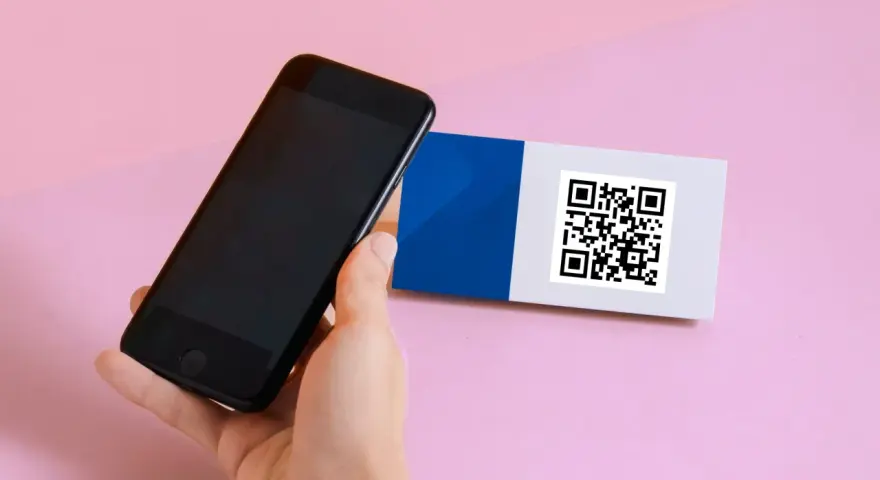 En hand håller en iPhone 6 för att scanna en QR-kod på ett kort med blått och vitt.