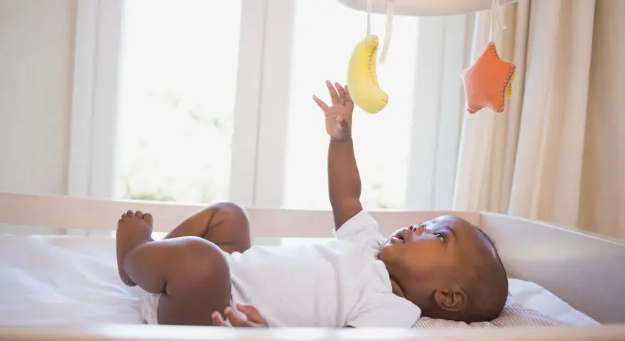 Maluch wyciąga rączkę do bananka i gwiazdki wiszących na karuzeli do łóżeczka.