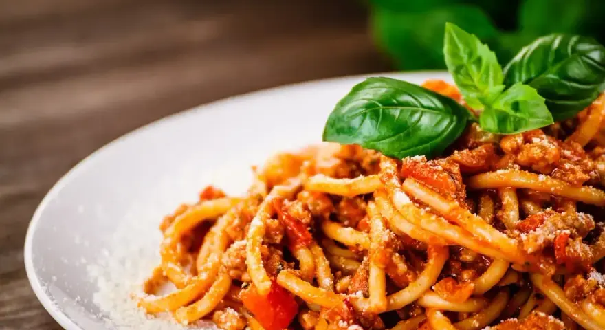 Prosty przepis na spaghetti z mięsem mielonym, podane na białym talerzu, ozdobione listkami bazylii i posypane parmezanem.