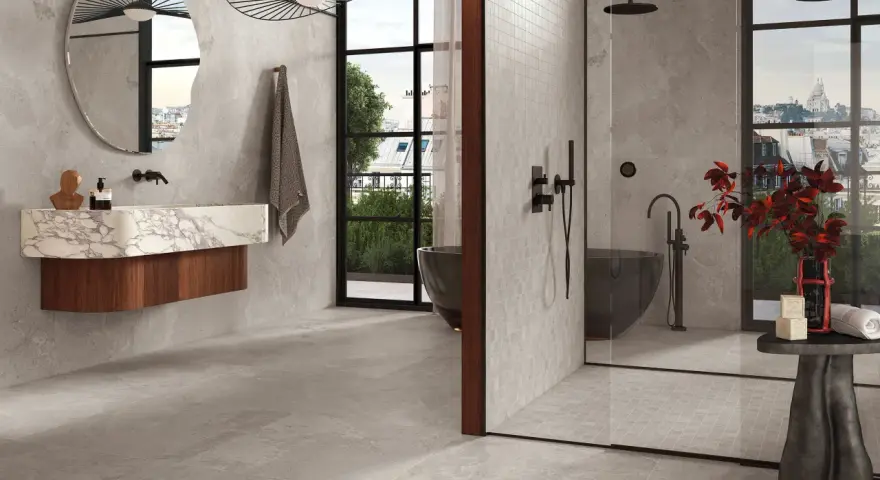Salle de bain moderne avec baignoire îlot et douche vitrée. Le sol et les murs sont recouverts de carrelage gris, tandis que la paroi de douche est en petite faïence.