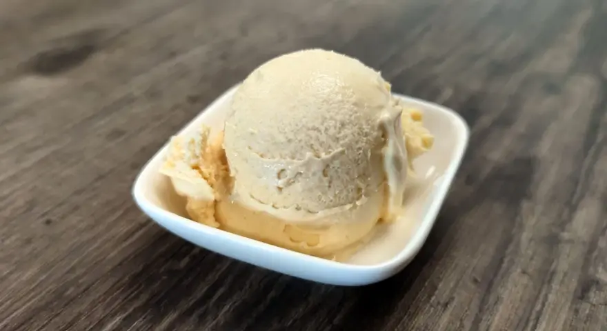 Cremiges Dulce de Leche Eis in einer weißen Schale auf Holzhintergrund.