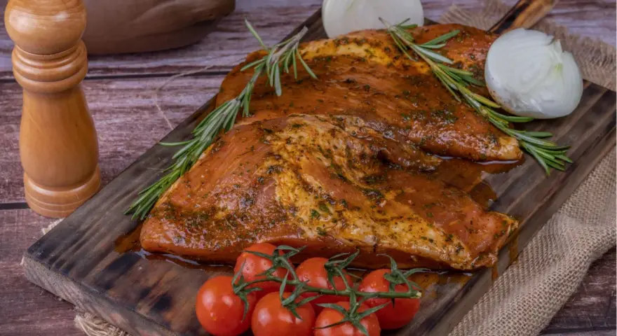 Carne marinada, lista para cocinar. El secreto ibérico se revela con romero, tomates y cebolla.
