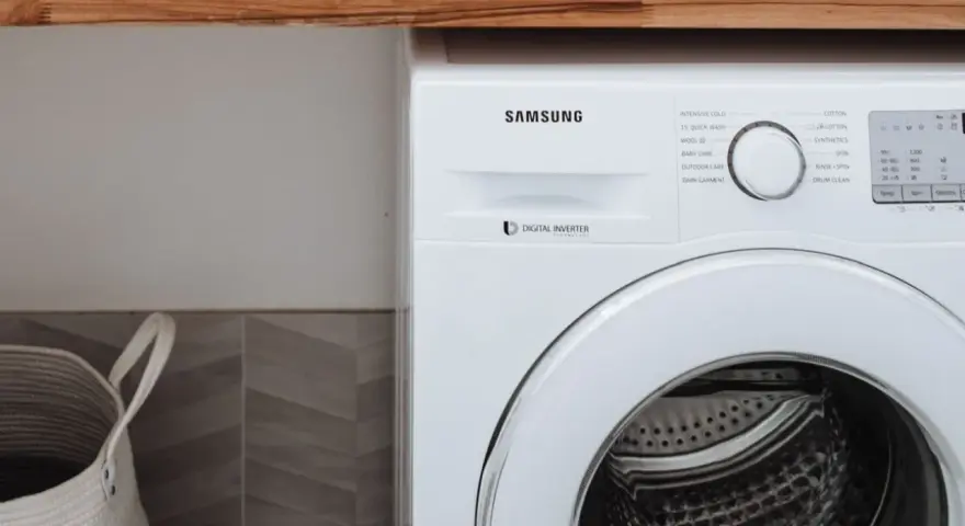 Biała pralka Samsung z technologią Digital Inverter. Obok kosz na pranie.