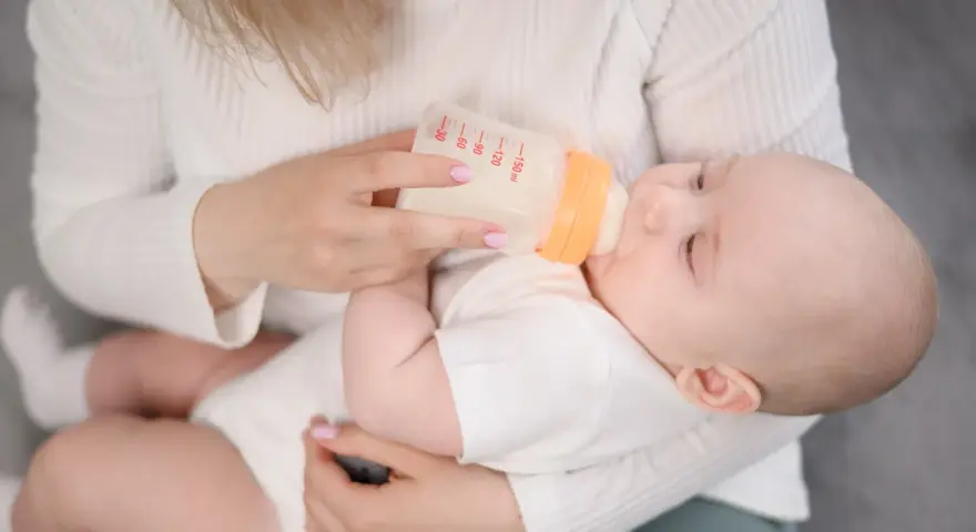 Mama karmi dziecko mlekiem modyfikowanym z butelki. Dziecko pije spokojnie, a mama czule go trzyma.