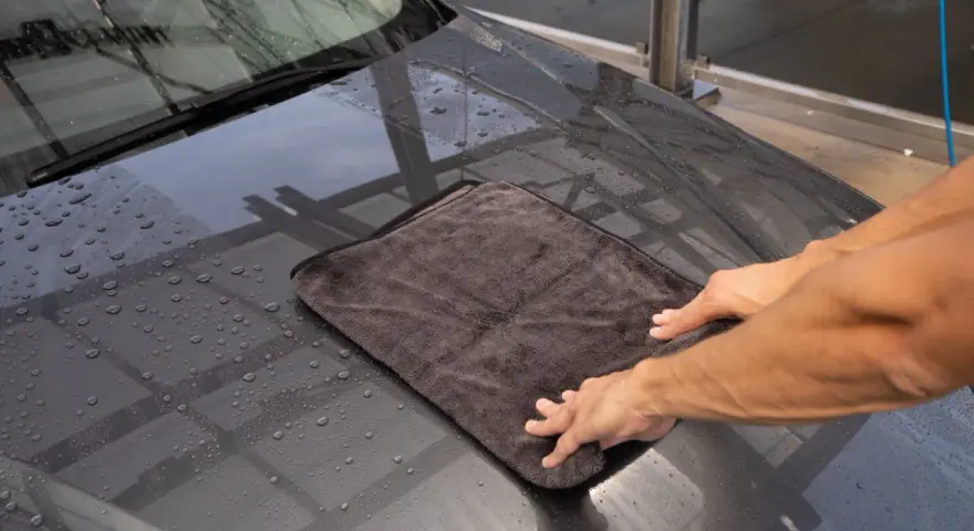 Hände trocknen mit einem Mikrofasertuch die Motorhaube nach der Autowäsche. Perfekt für das auto innenraum trocknen.