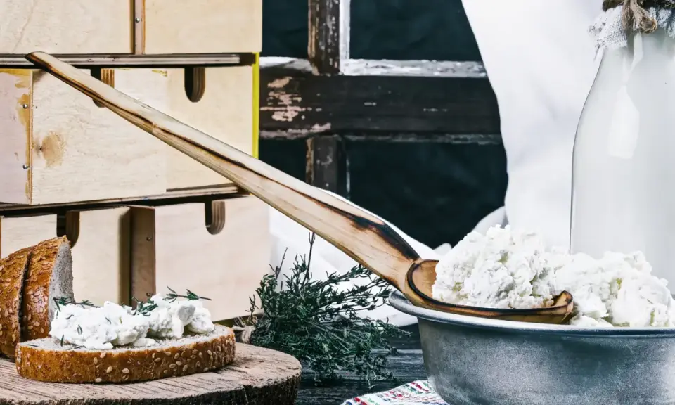 Fromage blanc frais, parfait pour une recette fromage blanc yaourtière. Servi sur du pain avec des herbes, à côté d'une bouteille de lait.