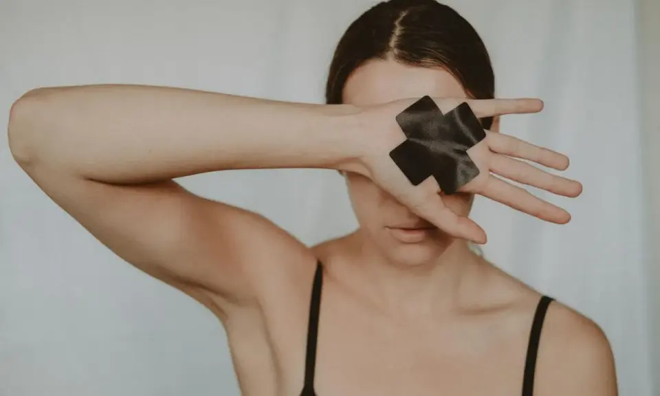 Dłoń z czarną taśmą w kształcie krzyża zakrywa oko, symbolizując traumę seksualną i potrzebę ochrony.