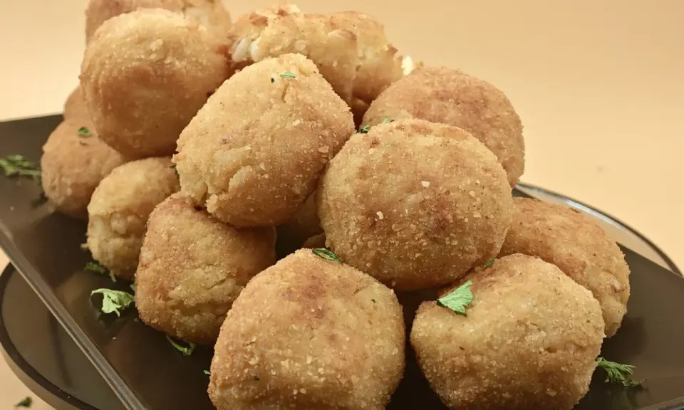Un mucchio invitante di polpette di riso dorate e croccanti, guarnite con prezzemolo fresco, su un piatto scuro.