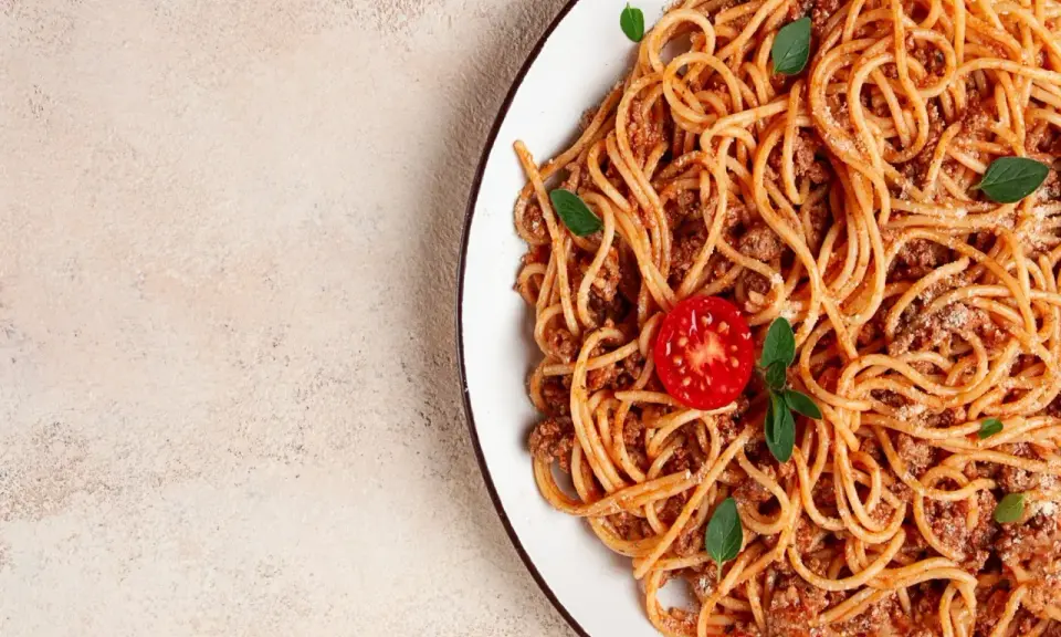 Pyszne spaghetti z mięsem mielonym, udekorowane pomidorkiem i listkami bazylii. Idealne na szybki obiad.
