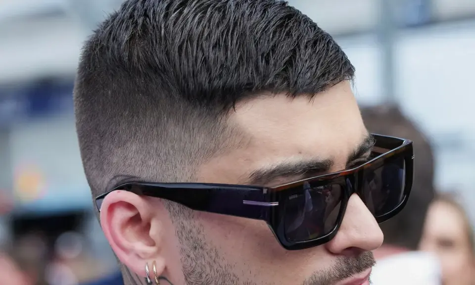 Mann mit stylischem Crew Cut und Sonnenbrille, der nachdenklich in die Ferne blickt.