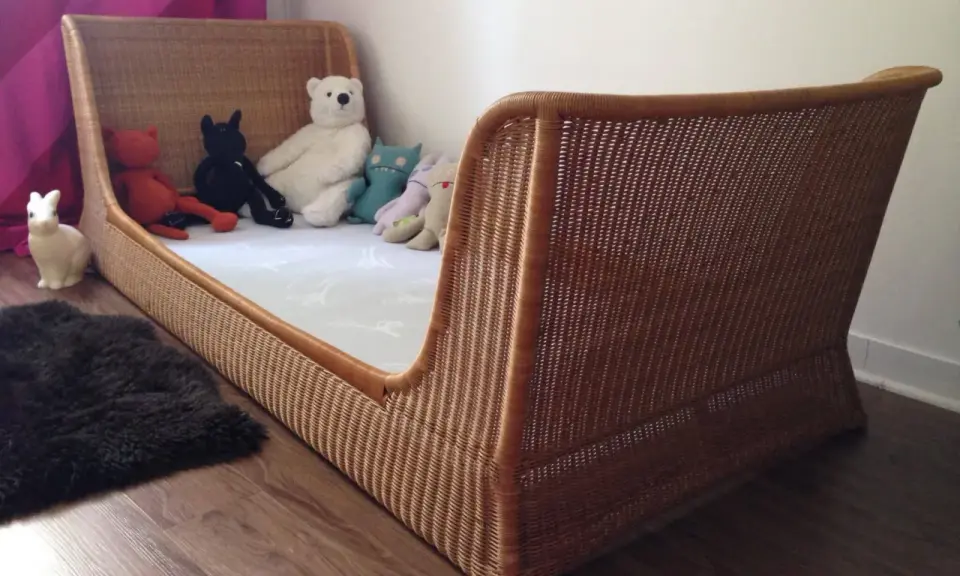 Lit en rotin tressé, style Louis Sognot, avec des peluches attendant patiemment dans un lit douillet.