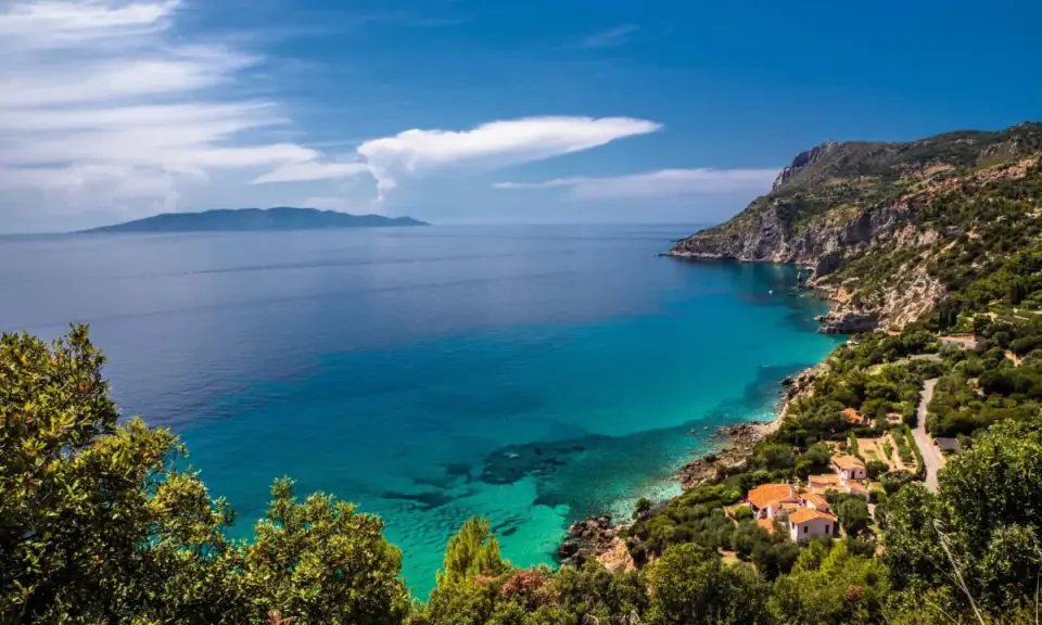 Un angolo di paradiso dove in Toscana c'è il mare. Acque cristalline lambiscono una costa rocciosa, con case dai tetti rossi immerse nel verde.