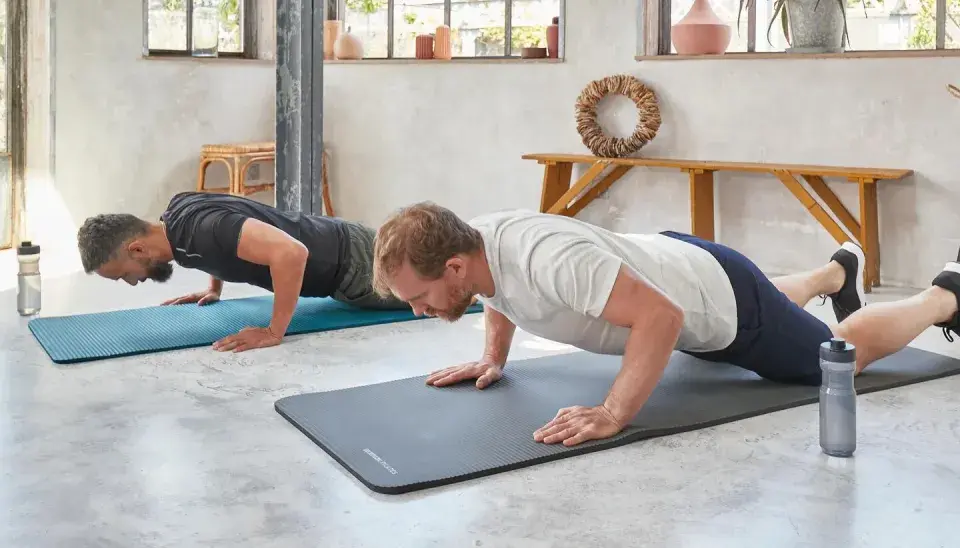 Dwóch mężczyzn wykonuje ćwiczenia na triceps w domu, robiąc pompki na matach.