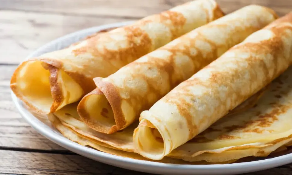 Gestapelte, gerollte Pfannkuchen ohne Mehl auf einem Teller. Sie sind goldbraun und sehen lecker aus.
