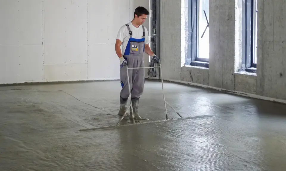 Pracownik wyrównuje świeżą wylewkę betonową na styropianie, dbając o jej minimalną grubość.