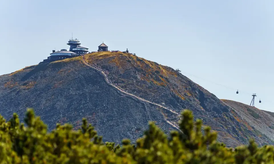 Szczyt Śnieżki w Karkonoszach, z obserwatorium i schroniskiem, po którym wije się ścieżka turystów. W tle kolejka linowa.