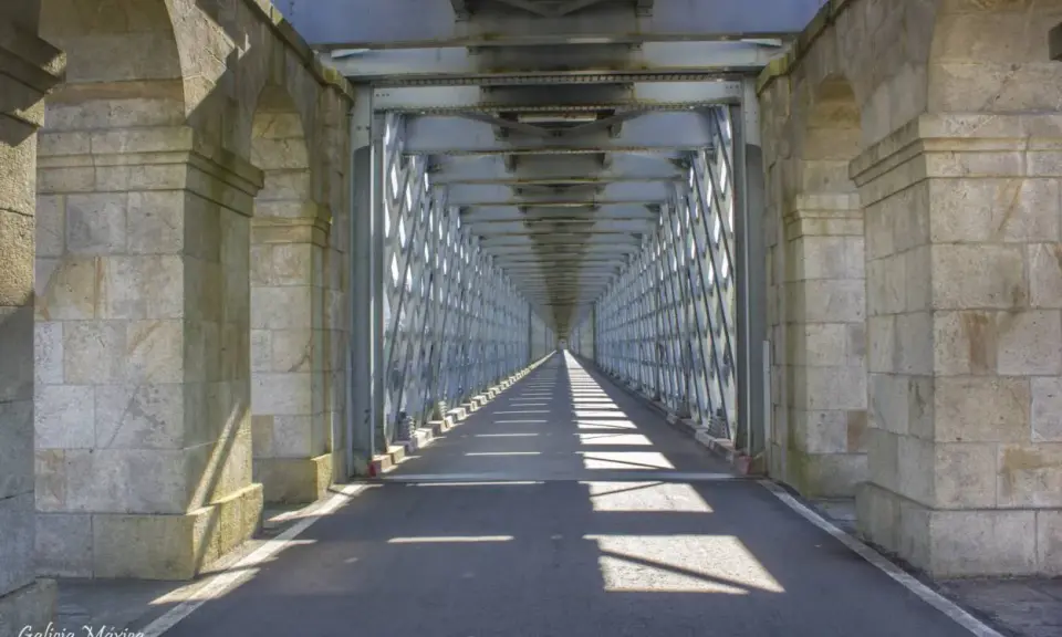 El **puente internacional Tui** se alza imponente, un túnel de metal y piedra que se pierde en la distancia, proyectando sombras geométricas sobre el asfalto.