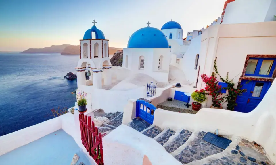 Białe domy z niebieskimi kopułami kościołów na tle morza i wysp. Widok na kaldera Santorini o zachodzie słońca.
