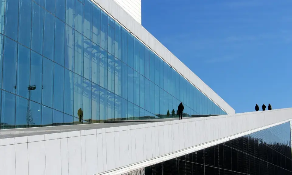 Nowoczesna architektura Uniwersytetu w Oslo z lustrzaną fasadą odbijającą niebo i ludzi.