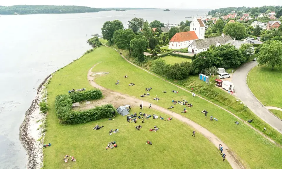 En grupp människor njuter av en paus under sin vandring i Danmark. En kyrka med tegeltak syns i bakgrunden.