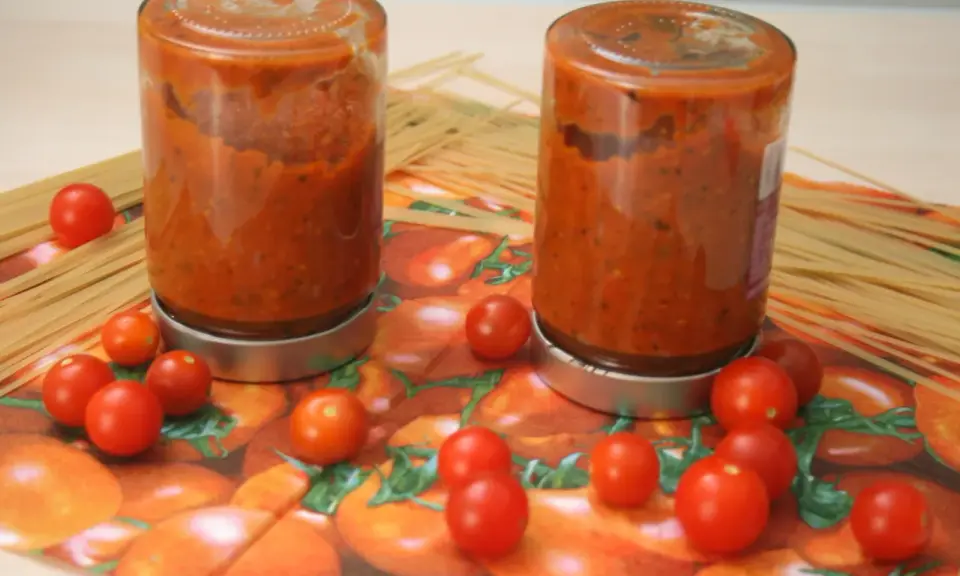 Zwei Gläser mit Tomatensoße, umgeben von frischen Tomaten und Spaghetti. Perfekt für die Tomaten haltbar machen.