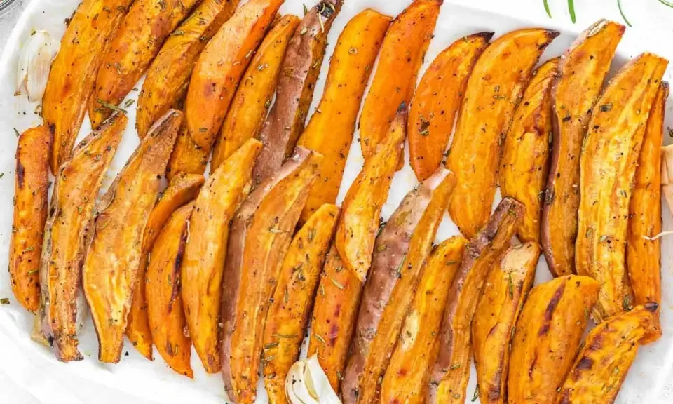 Patate dolci al forno, tagliate a spicchi e condite con erbe aromatiche, servite su un piatto bianco.