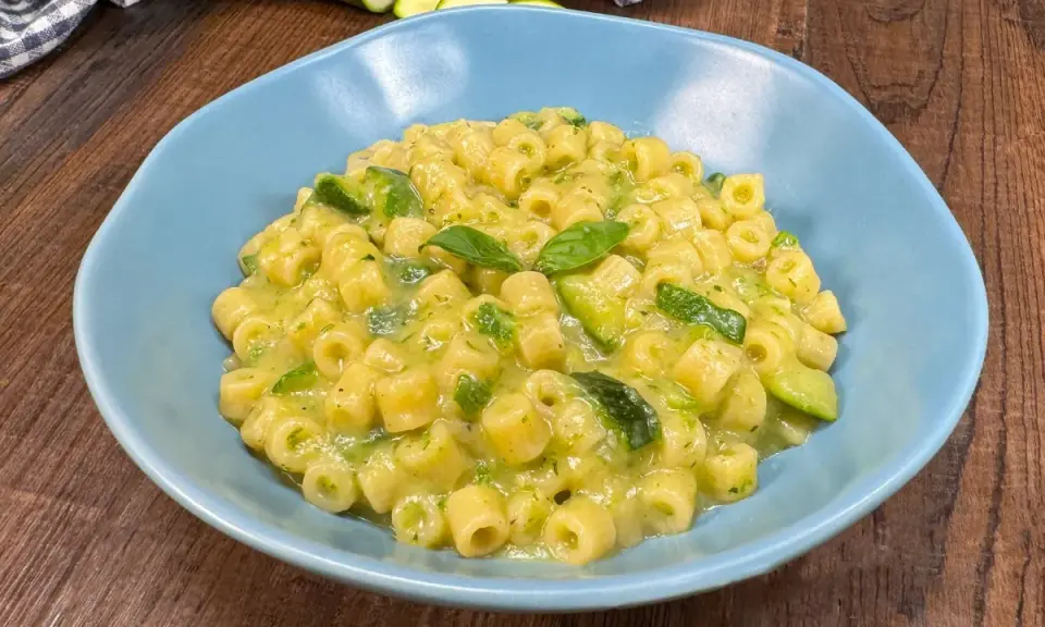Un piatto di pasta con zucchine e basilico, cremoso e invitante, servito in una ciotola azzurra su un tavolo di legno.