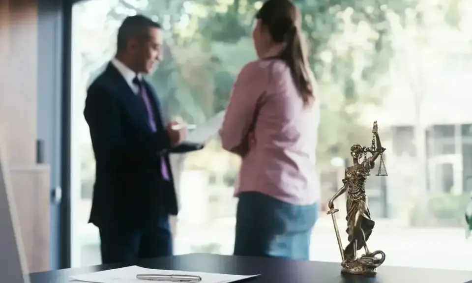 Mecenas, kto to? Prawnik w garniturze rozmawia z klientką przy biurku z figurką Temidy.