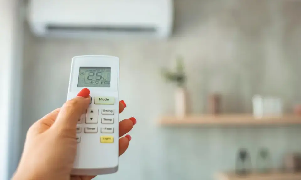 Mano con control remoto ajustando el aire acondicionado, buscando la temperatura ideal.