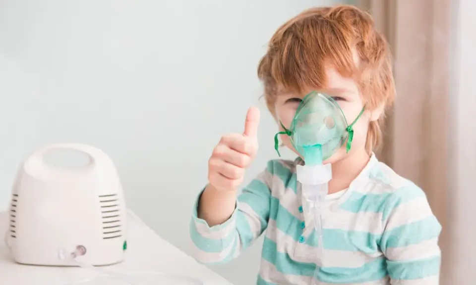 Chłopiec z gorączką i przyspieszonym oddechem używa nebulizatora, pokazując kciuk w górę.