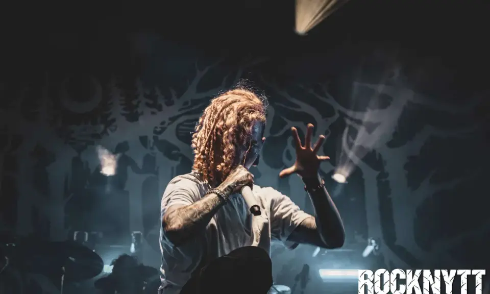 Lorna Shore Sverige: Sångaren med flammigt hår och tatueringar greppar mikrofonen på scenen, omgiven av rök och dramatiskt ljus.