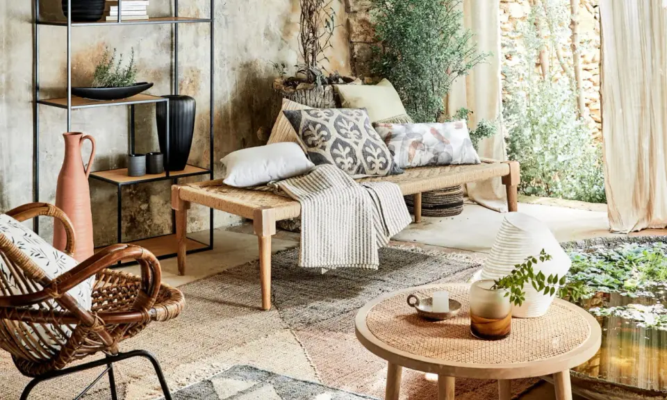 Un salon sans canapé, avec un banc tressé, des coussins décoratifs, un fauteuil en rotin et une étagère murale.