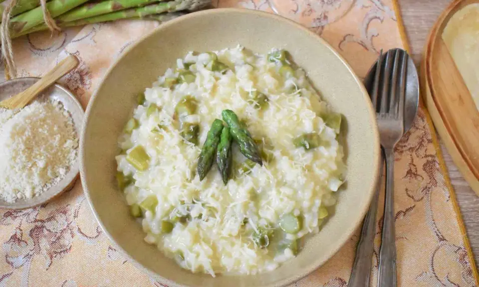 Kremowe risotto ze szparagami, posypane parmezanem, z kilkoma zielonymi szparagami na wierzchu.
