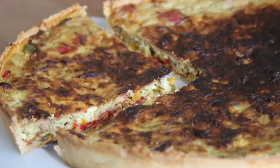 Une part de quiche poivron feta dorée, avec des morceaux de poivrons colorés et de feta crémeuse dans sa garniture.