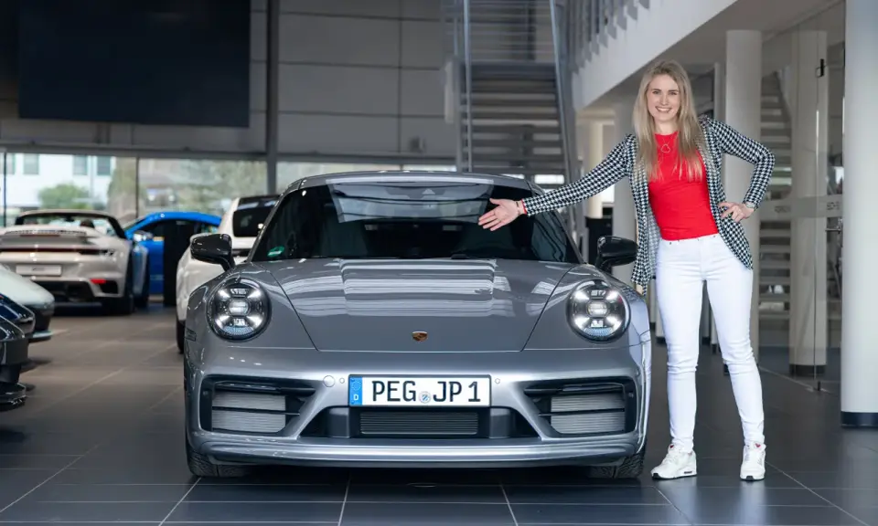 Eine Frau präsentiert stolz einen grauen Porsche Carrera T. Die Wertentwicklung dieses Sportwagens ist ein spannendes Thema für Enthusiasten.