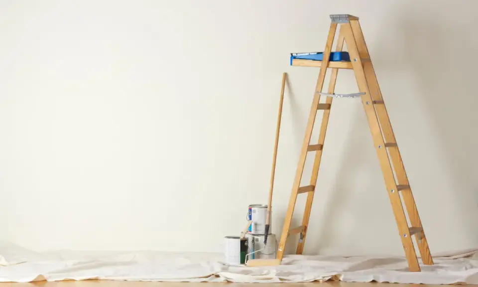 Préparation pour peindre une chambre : échelle en bois, pots de peinture, rouleau et bâton sur une toile de protection.