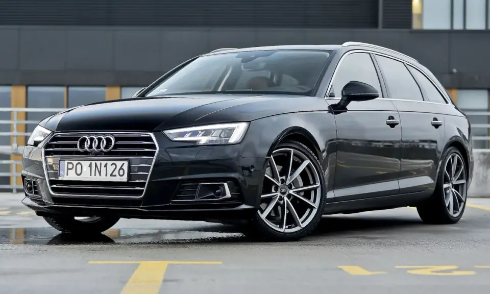 Czarny Audi A4 Avant, model b9, zaparkowany na mokrym parkingu z żółtymi liniami.
