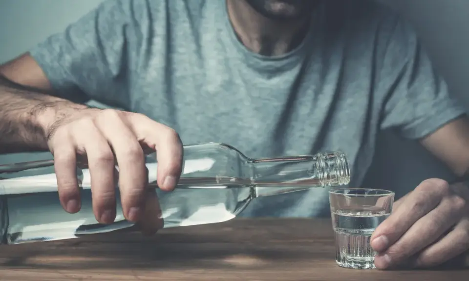 Mężczyzna nalewa alkohol do kieliszka. Nadmierne spożycie alkoholu negatywnie wpływa na żyły, prowadząc do ich uszkodzenia.