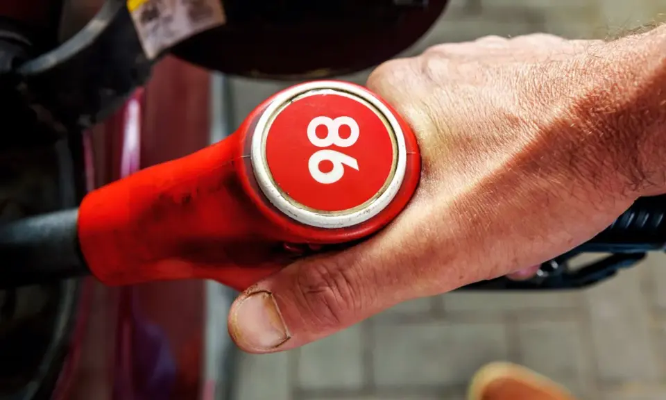 Mano sujetando una boquilla de gasolina roja con el número 96, indicando uno de los tipos de gasolina en España.