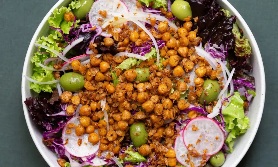 Ensalada colorida con garbanzos fritos crujientes, aceitunas verdes, lechugas variadas, rábano y cebolla morada.