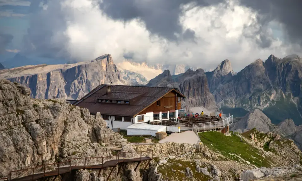Rifugio alpino con terrazza panoramica, uno dei migliori rifugi dove dormire Dolomiti, incastonato tra imponenti vette rocciose e nuvole minacciose.